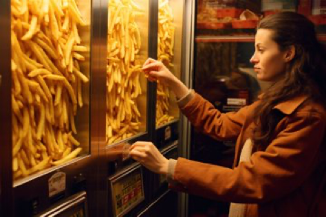 Woman operating enormous french fries vending machine, closeup photograph --ar 3:2