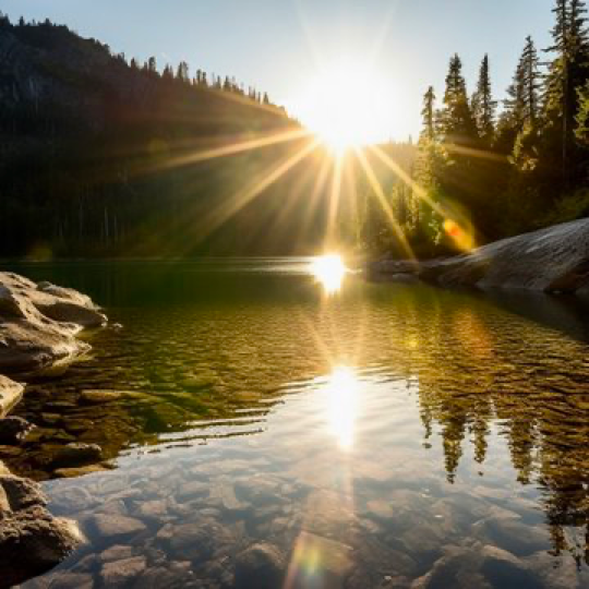 photo of sun flare reflecting in a serene mountain lake at sun rise --v 5
